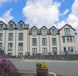 A multi-story residential building with balconies and dormer windows under a blue sky with clouds at Sandy Bay Retreat in Benllech