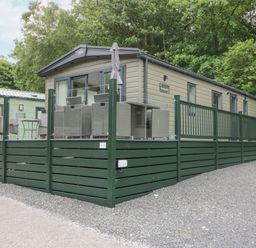 An exterior view of a mobile home with a green fenced deck and outdoor furniture at Mon in Troutbeck Bridge