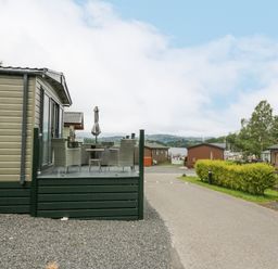 Outdoor seating area with table and chairs next to caravan homes near a road and lake view