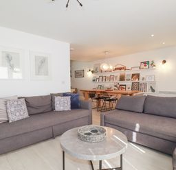 A living room with two gray sofas and a round coffee table with a wicker tray and a dining area with a wooden table and black chairs at Tincroft in Porthtowan
