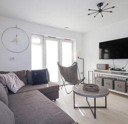 A living room with a grey sofa cushions a butterfly chair a round coffee table a wall clock a flat screen tv and a storage unit at Tincroft in Porthtowan
