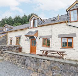 The exterior of a stone cottage with wooden framed windows a wooden door and a picnic table at Llys-y-Wennol in Penmachno