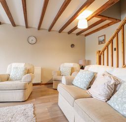 A living room with beige armchairs and sofa with cushions wooden beams on ceiling and wooden staircase at Llys-y-Wennol in Penmachno