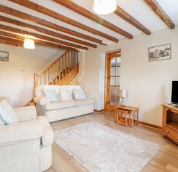 A living room with two beige sofas a wooden staircase a wooden tv cabinet with a television a wooden side table with a lamp and a rug on the floor at Llys-y-Wennol in Penmachno