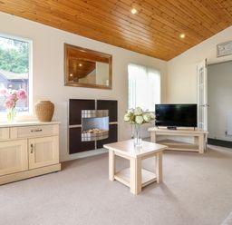 A living room with a wooden ceiling a fireplace a television on a stand and a table with flowers at Lodge 3 At Pound Farm in Crook near Kendal