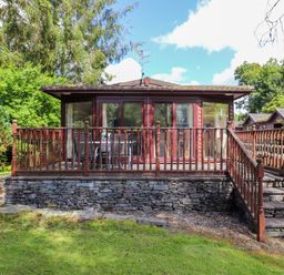 A wooden lodge with a raised stone foundation and a wooden deck surrounded by trees at Lodge 7 At Pound Farm in Crook near Kendal