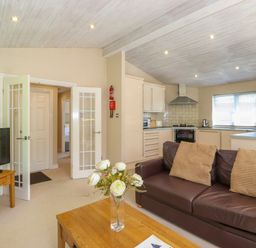 A living room with a brown sofa, wooden coffee table with flowers, television on a stand and an open doorway at Lodge 7 At Pound Farm in Crook near Kendal