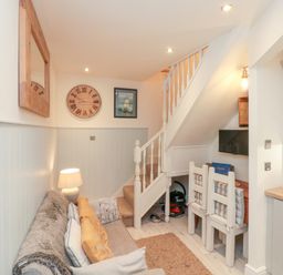 A small living area with a sofa pillows lamp wall clock and framed picture next to a staircase with two chairs and a television under the stairs at Little Gem in Whitby
