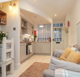 A kitchen and living area with cabinets chairs sofa with pillows and a door at Little Gem in Whitby