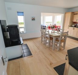 A dining area with a white table and chairs next to a kitchen with wooden cabinets and a black stove in a house at Cois Leice Cushlecka near Mulranny County Mayo