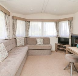 A living room with a beige sofa corner cushions small television and stool at 23 Manleigh Park in Combe Martin