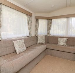 An L shaped sofa with floral cushions in a room with corner windows and floral curtains at 23 Manleigh Park in Combe Martin