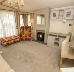 A living room with plaid armchairs and ottoman a fireplace and a wall cabinet at The Boathouse in East Wittering