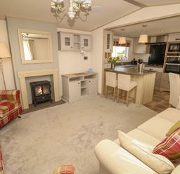 A living room with a fireplace armchairs sofas and a kitchen island with bar stools at The Boathouse in East Wittering