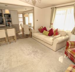 A living room with beige sofa and armchairs next to a dining area and kitchen at The Boathouse in East Wittering