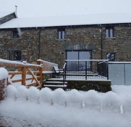 A house covered in snow with a railing and steps at Y Stabl in Cerrigydrudion