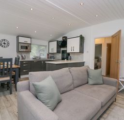 An open plan kitchen and living area with a sofa in front and a dining table with chairs near the kitchen at Don's Lodge in Grasmere 3 White Cross Bay near Windermere