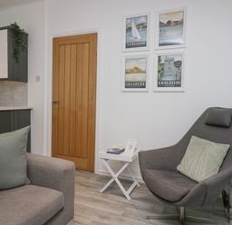 A living room with a gray armchair and sofa with pillows wooden door and framed pictures on the wall at Don's Lodge Grasmere 3 White Cross Bay near Windermere