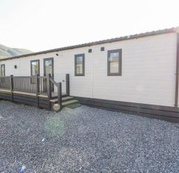 An exterior view of a single-story building with a gravel foreground and a wooden deck railing at Saorsa in St Fillans