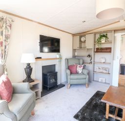 A living room with armchairs a television above a fireplace shelves and a wooden coffee table at Saorsa in St Fillans