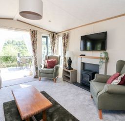A living room with armchairs a coffee table a TV above a fireplace and glass doors opening to an outdoor patio at Saorsa in St Fillans