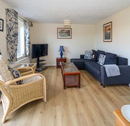 A living room with a TV angled in the corner a dark sofa with patterned cushions a wicker chair with cushions and floral curtains at 74 Reap Lane Southwell near Weston