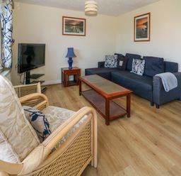 A living room with a dark blue sofa wooden coffee table wooden side table with blue lamp armchair with cushions and a television at 74 Reap Lane Southwell near Weston