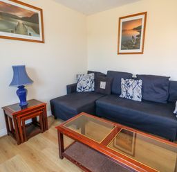 A living room with a dark sofa cushions tables a blue lamp and framed pictures on the wall at 74 Reap Lane Southwell near Weston