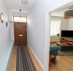 A hallway with a wooden front door and three circular mirrors on the wall leading to a living room with a television and wooden coffee table at Bryn Siriol in Narberth