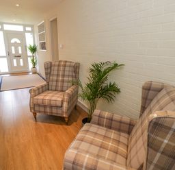 A hallway with two plaid armchairs a plant a doormat and a front door at Fenny Marina Cottage in Fenny Bentley