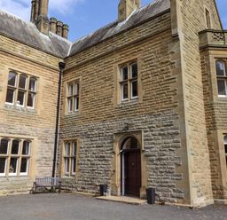 The exterior of a stone building with multiple windows a wooden bench and a dark wooden door at North Wing in Middleton Hall Estate near Belford