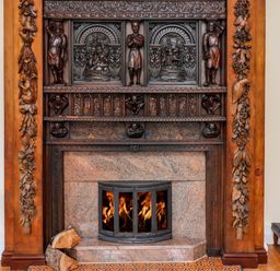 A fireplace with intricate wooden carvings and a fire burning inside at North Wing in Middleton Hall Estate near Belford