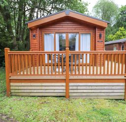 A wooden cabin with a porch and patio furniture surrounded by grass and trees at Tawny Owl Lodge Coniston 4 White Cross Bay near Windermere