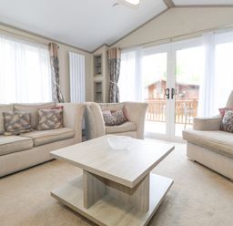A living room with beige sofas and a wooden coffee table near glass doors at Tawny Owl Lodge in Coniston 4 White Cross Bay near Windermere