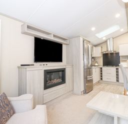 An open living area with a wall-mounted television above an electric fireplace a beige armchair a stainless steel refrigerator a kitchen with cabinets and a dining table with chairs at Tawny Owl Lodge Coniston 4 White Cross Bay near Windermere