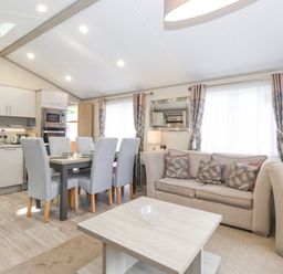 A living room and kitchen area with a dining table and chairs a beige sofa and armchair at Tawny Owl Lodge Coniston 4 White Cross Bay near Windermere