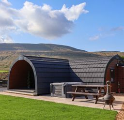 An outdoor area with a curved wooden cabin a picnic table and a chiminea on a paved patio at Lapwing in Chapel Le Dale near Ingleton