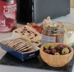 A slate serving board with crackers, a jar of chutney, a wooden bowl of olives, cheese, and cured meats on a kitchen countertop at Oyster Catcher in Chapel Le Dale near Ingleton