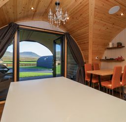 A wooden interior pod with a dining table and orange chairs next to open glass doors showing an outdoor view at Heron in Ingleton