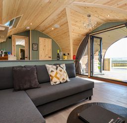 A living area with a gray sofa and pillows wooden ceiling and walls and large open glass doors at Wren in Ingleton