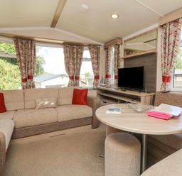 A living room with beige sofas and a round table with a television and patterned curtains at 25 Manleigh Park in Combe Martin