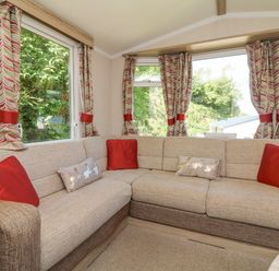 A corner sofa with red and beige cushions by windows with patterned curtains at 25 Manleigh Park in Combe Martin