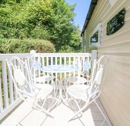 A small outdoor balcony with white metal table and chairs surrounded by white railing and greenery at 25 Manleigh Park in Combe Martin