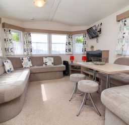 A living room with beige sofas cushions a table stools a wall mounted TV and windows at 26 Manleigh Park in Combe Martin