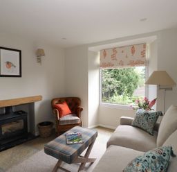 A living room with a fireplace armchair sofa and a window with a view of trees at Little Robin Cottage in Ambleside