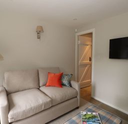 A living room with a beige sofa and two cushions a wall-mounted tv and a door at Little Robin Cottage in Ambleside