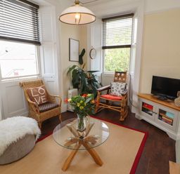 A sitting room with two chairs a glass coffee table a television on a wooden cabinet and a plant at Belmont House in Bowness-On-Windermere