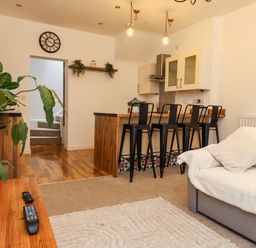 A living room with a sofa and kitchen area with bar stools at Hole in the Wall in Caernarfon