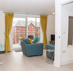 A living room with teal sofas yellow curtains and a small dining table near a glass door at Rolles Rainbow in Exmouth