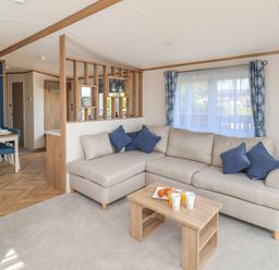 A living room with a beige sofa and blue cushions next to a wooden table with drinks and pastries at Aspen Lodge in Whitby